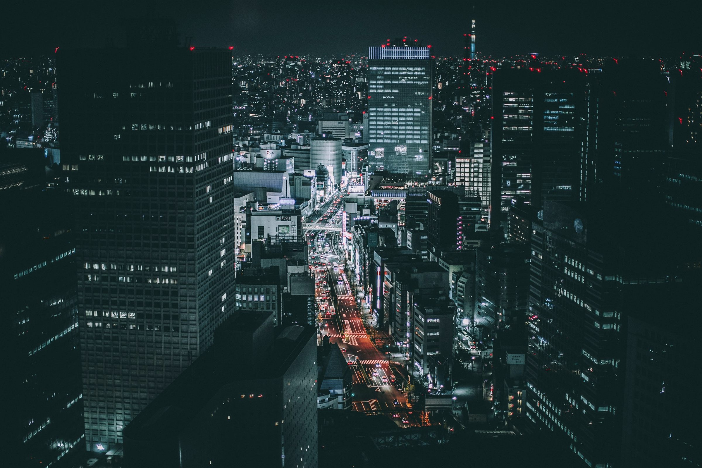 Dark aerial of Tokyo office towers and lit avenue at night