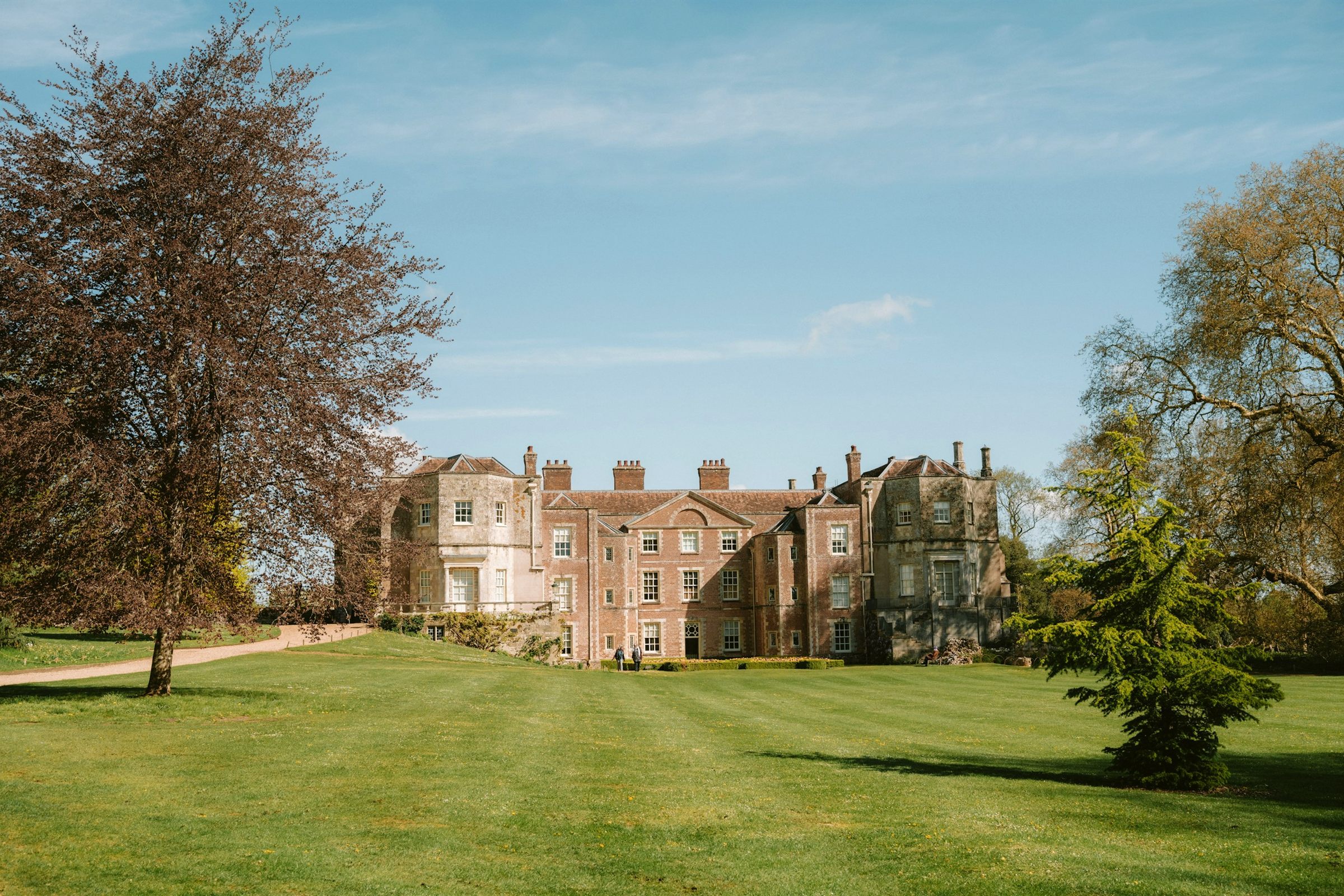Historic red-brick manor house beyond a green lawn and trees