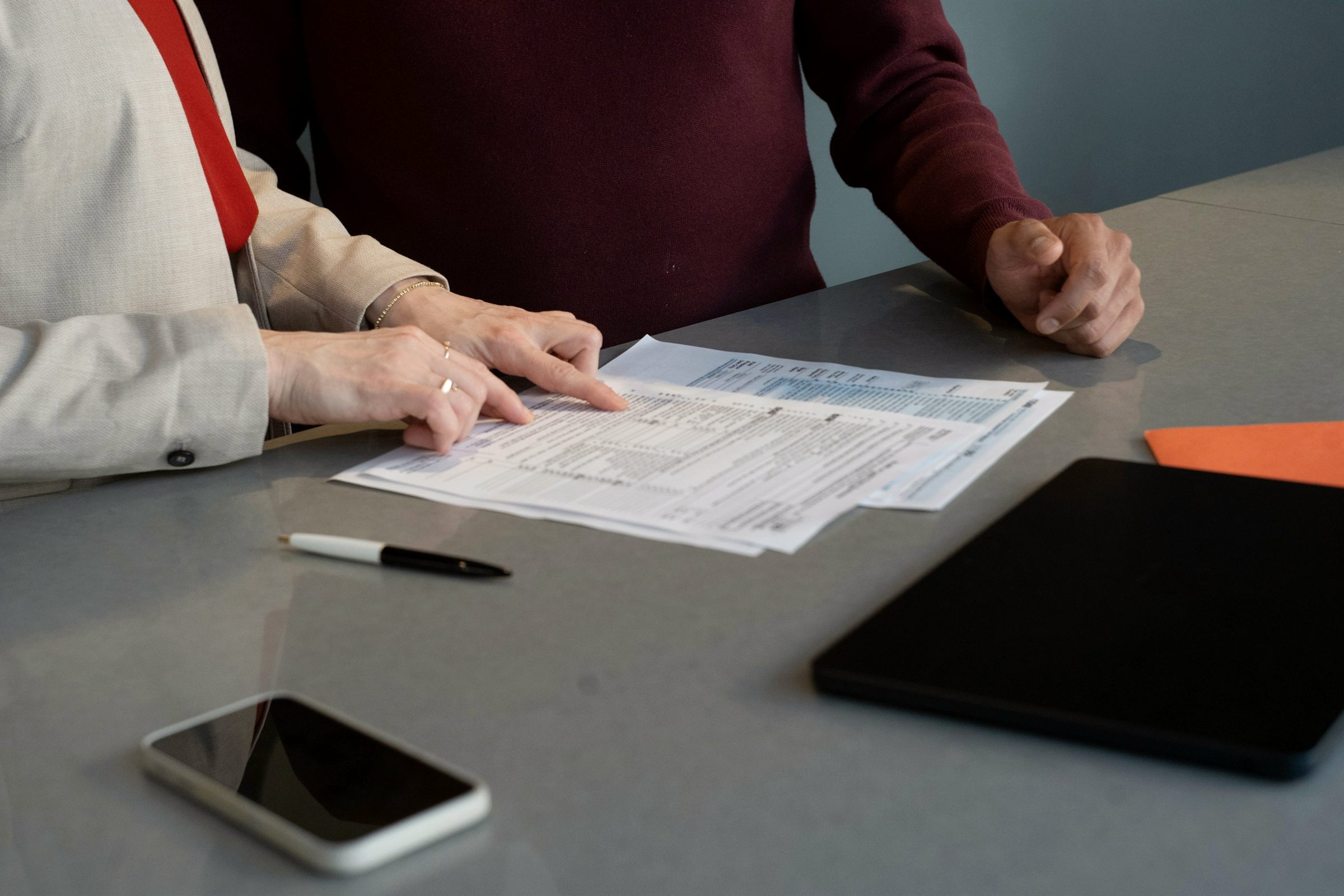 Two people reviewing a payment form together at a grey desk, hands only