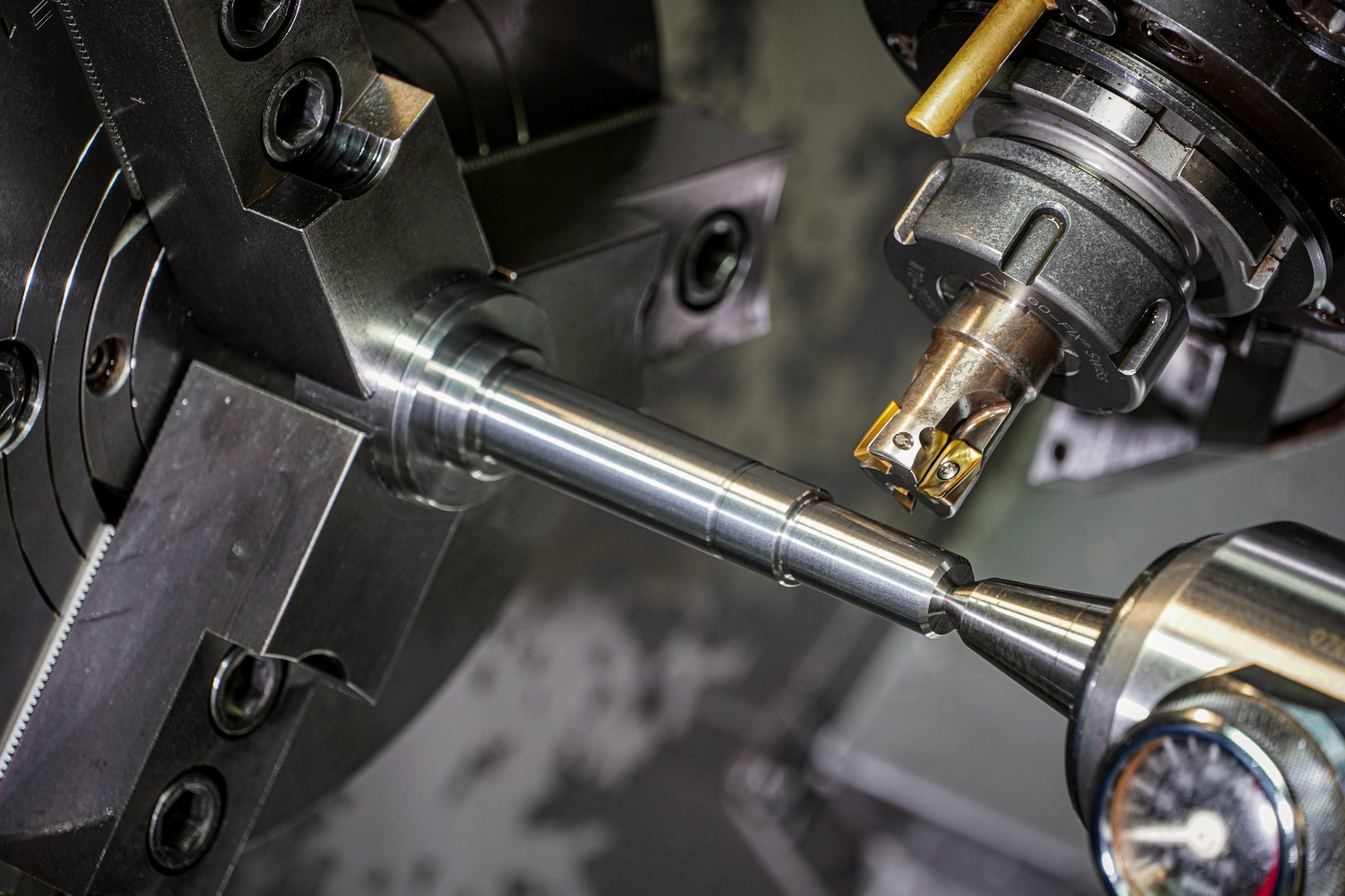 Metal rod being machined in a lathe chuck, dark industrial close-up